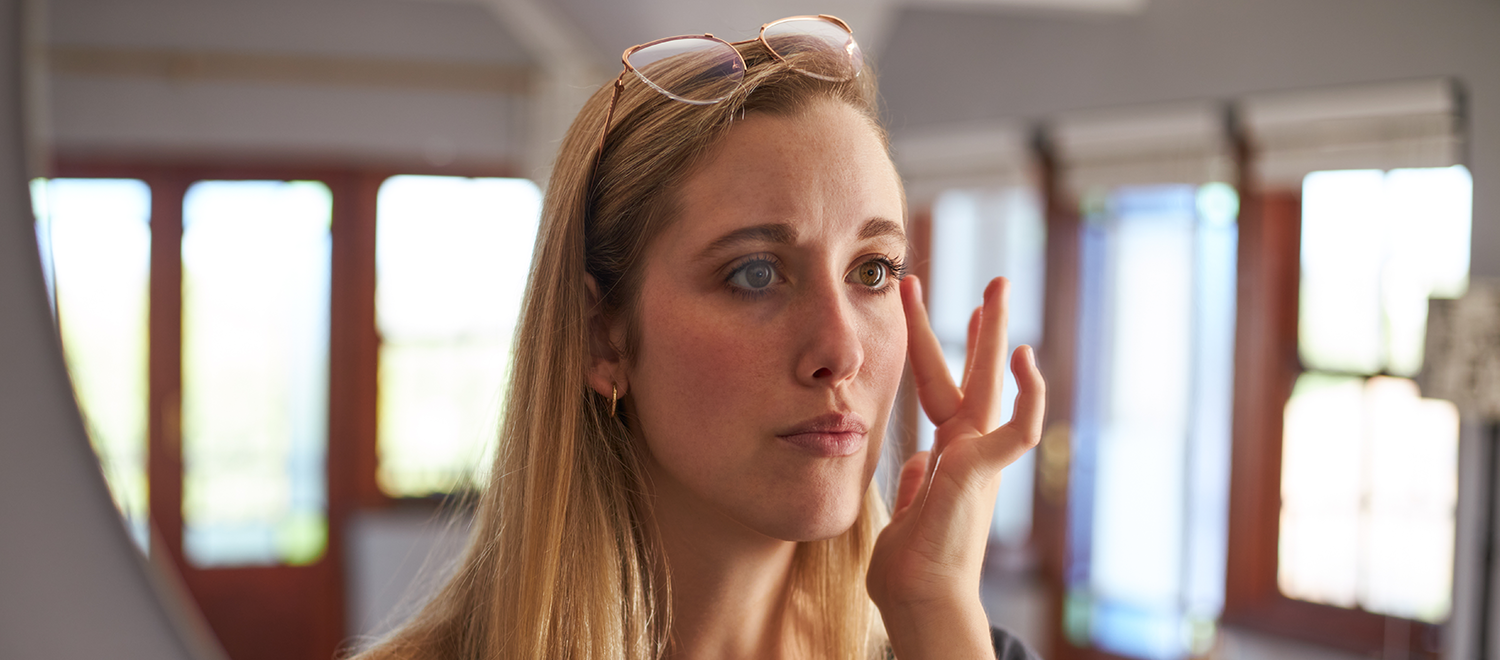 Woman examining her face in a mirror, representing skin changes and symptom awareness associated with breast implant illness