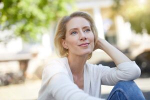 Relaxed middle-aged woman sitting outdoors with short hair, representing recovery from hair loss after breast augmentation or implant removal
