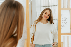 A woman smiling at her reflection in the mirror, representing positive breast explant before and after results and a return to natural body comfort.