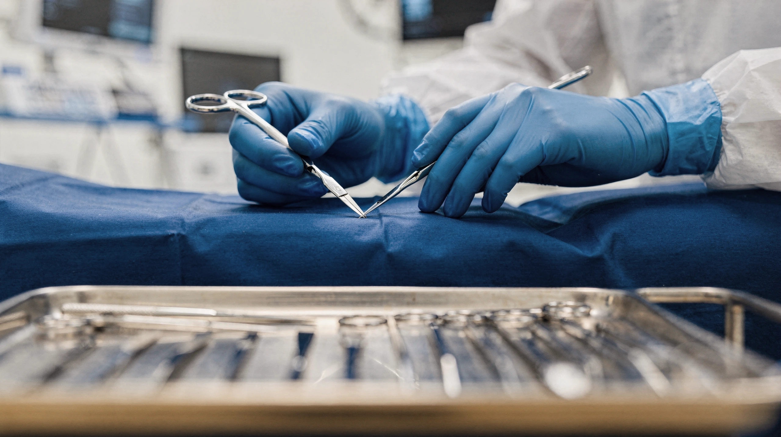 Surgeon's gloved hands holding surgical instruments during en bloc removal procedure on operating table