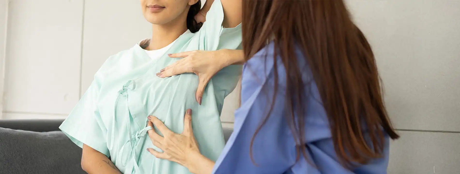 Healthcare provider examining patient's chest area while patient wears a light blue medical gown