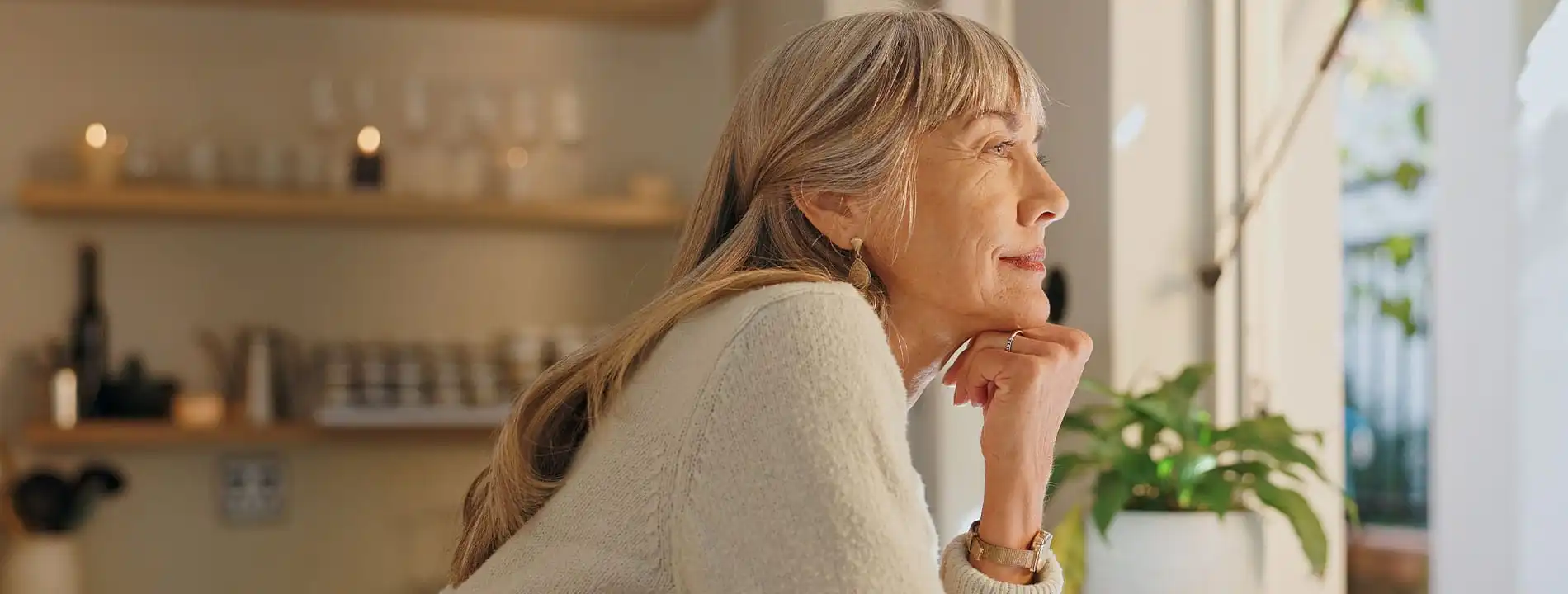 Mature woman with long hair gazing thoughtfully in a well-lit modern home interior