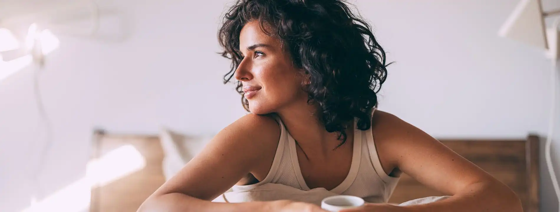 Young woman with curly dark hair smiling while resting on her elbows indoors