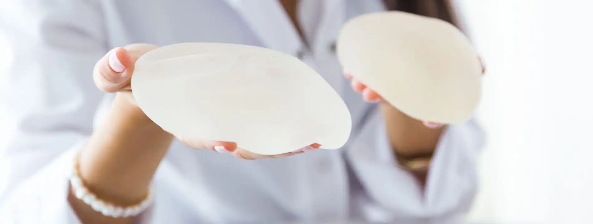 Healthcare provider in white coat holding two breast implant samples