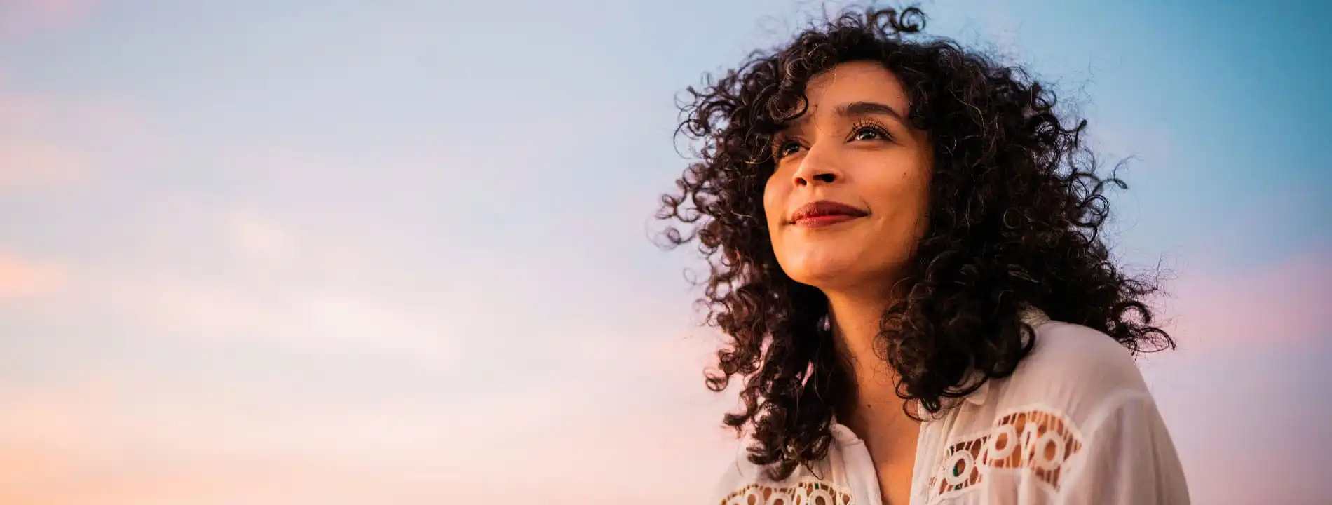 Woman with curly dark hair looking upward against a sunset sky