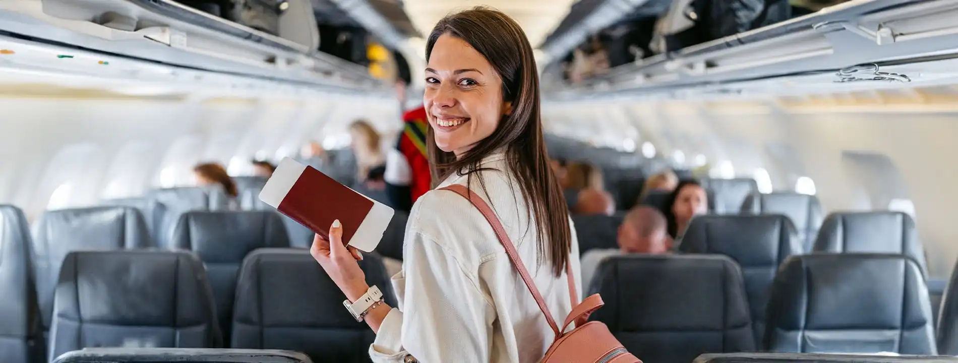 Woman smiling on an airplane holding a passport, turning toward camera