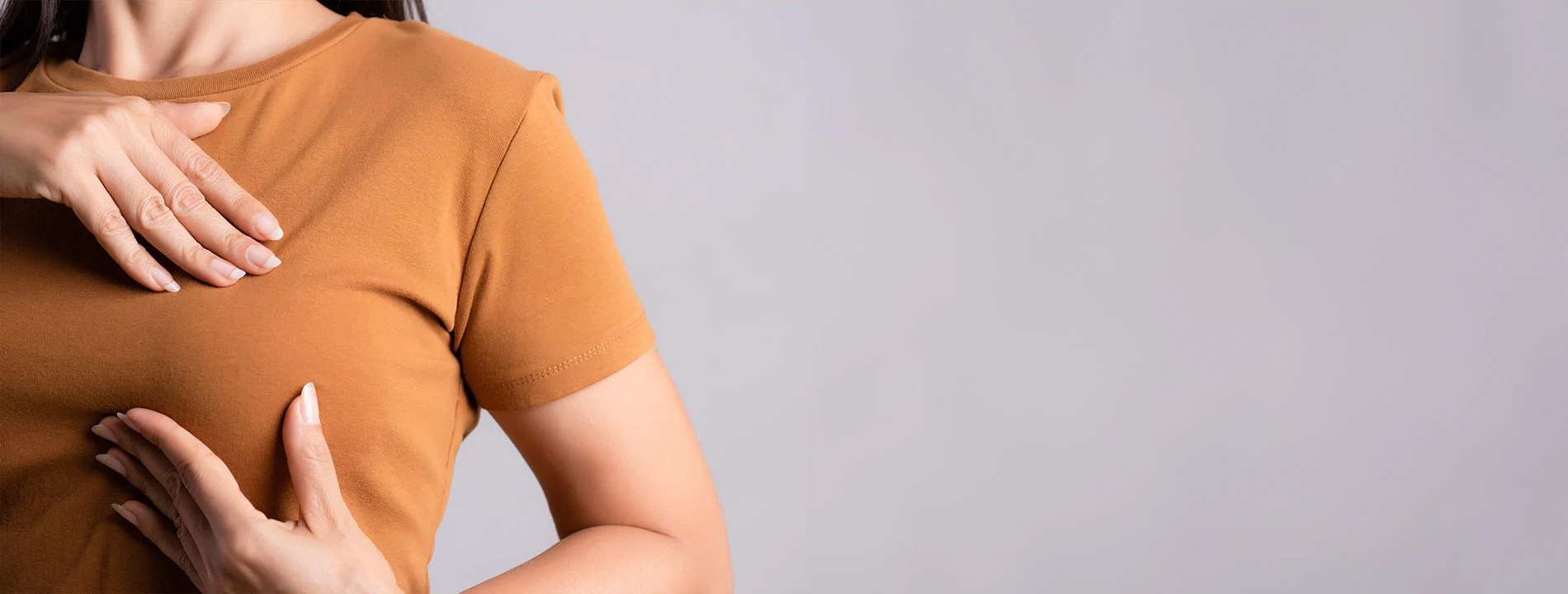 Person in orange shirt with hands on shoulder and torso area against light background
