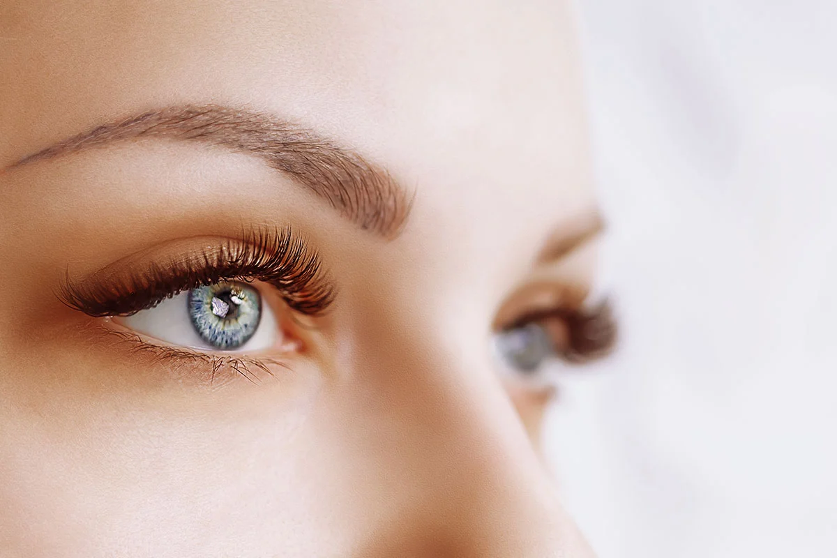 Close-up of woman's eye with full lashes and defined brow, shown in profile