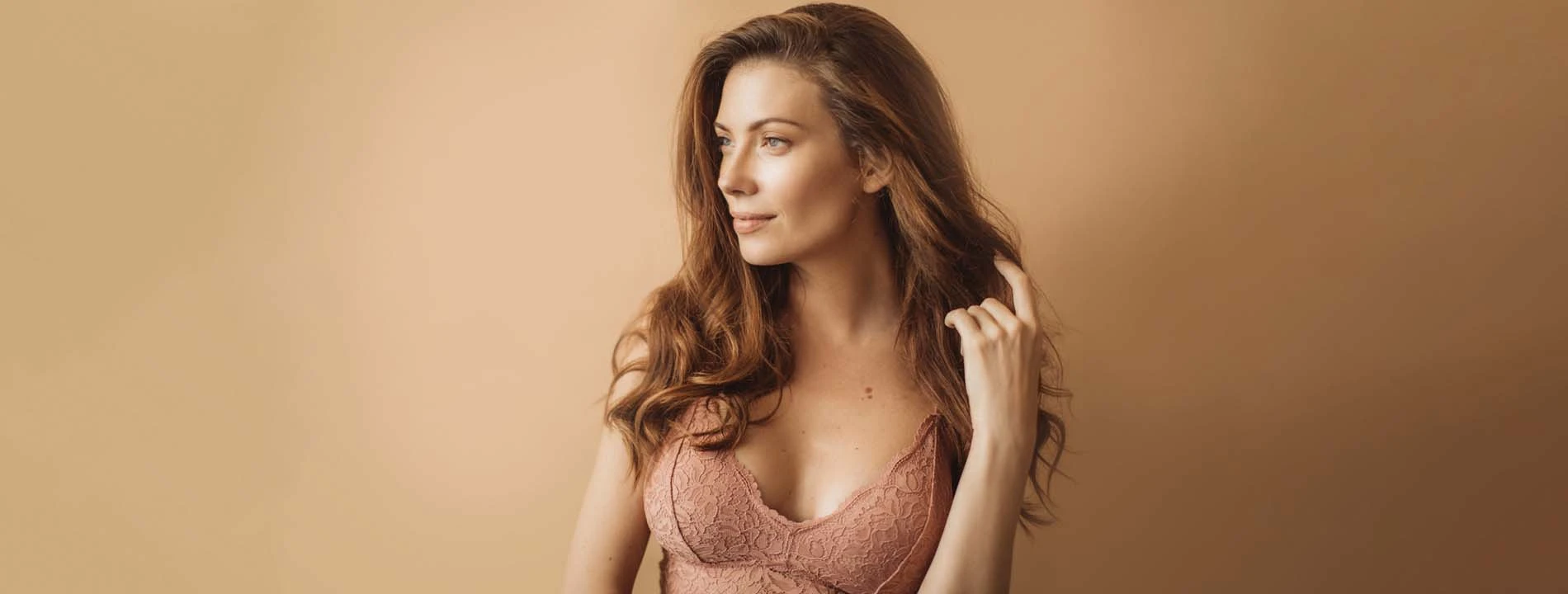Woman with long brown hair touching her hair against neutral background