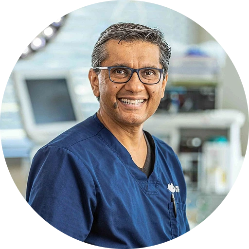 Dr. Shaher smiling in surgical scrubs and glasses in a clinical setting