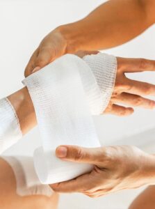 Hands wrapping white gauze bandage around an injury on a person's hand