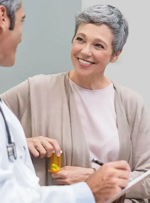 Smiling middle-aged woman receiving medication bottle from doctor in white coat