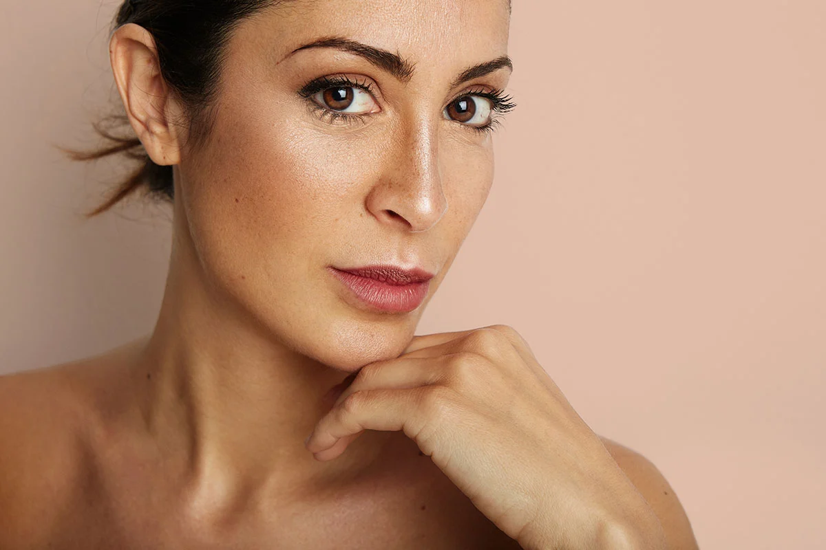 Woman in profile with hand on chin against neutral beige background