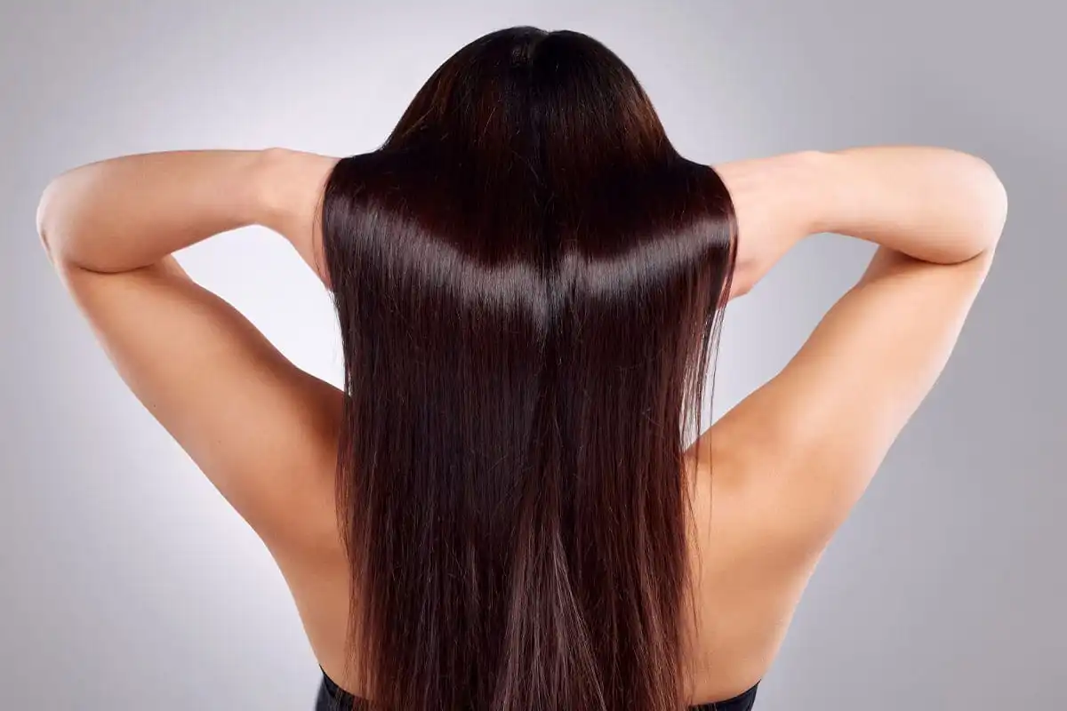 Woman from behind with hands behind head displaying full, dark, long hair