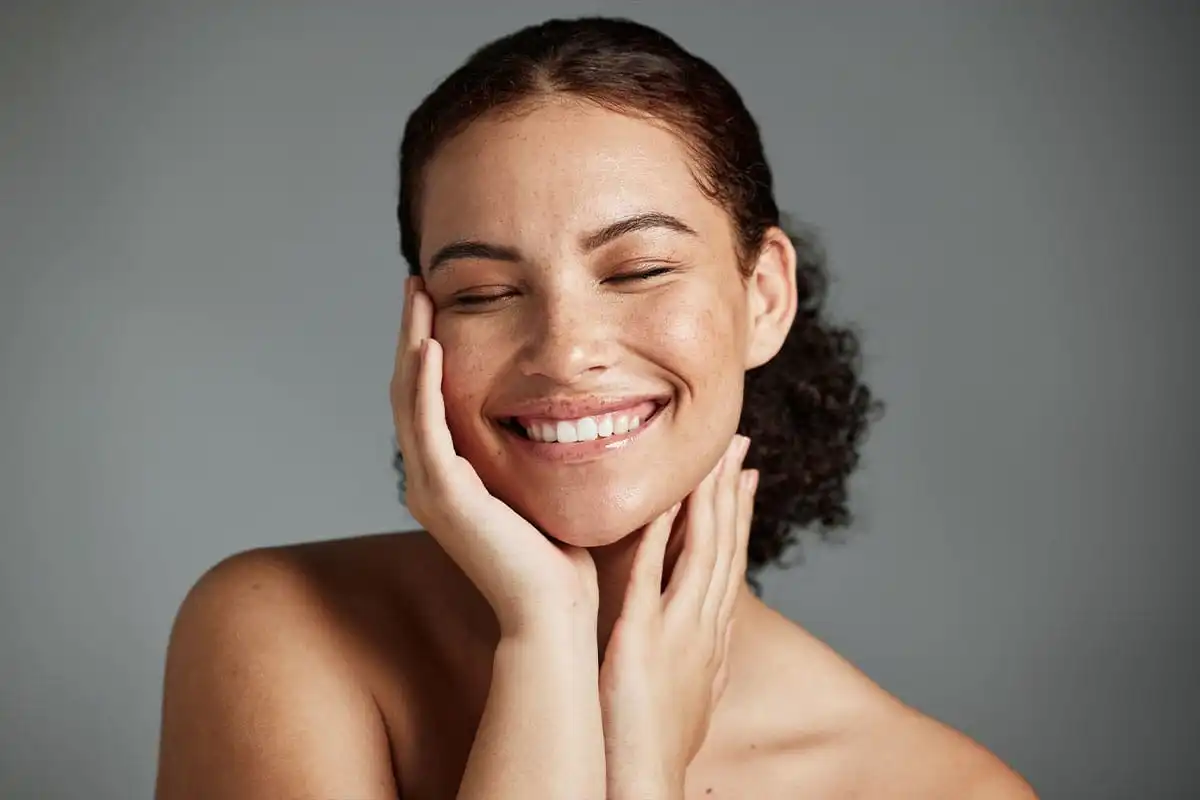 Woman smiling with hands touching face, displaying clear, radiant skin