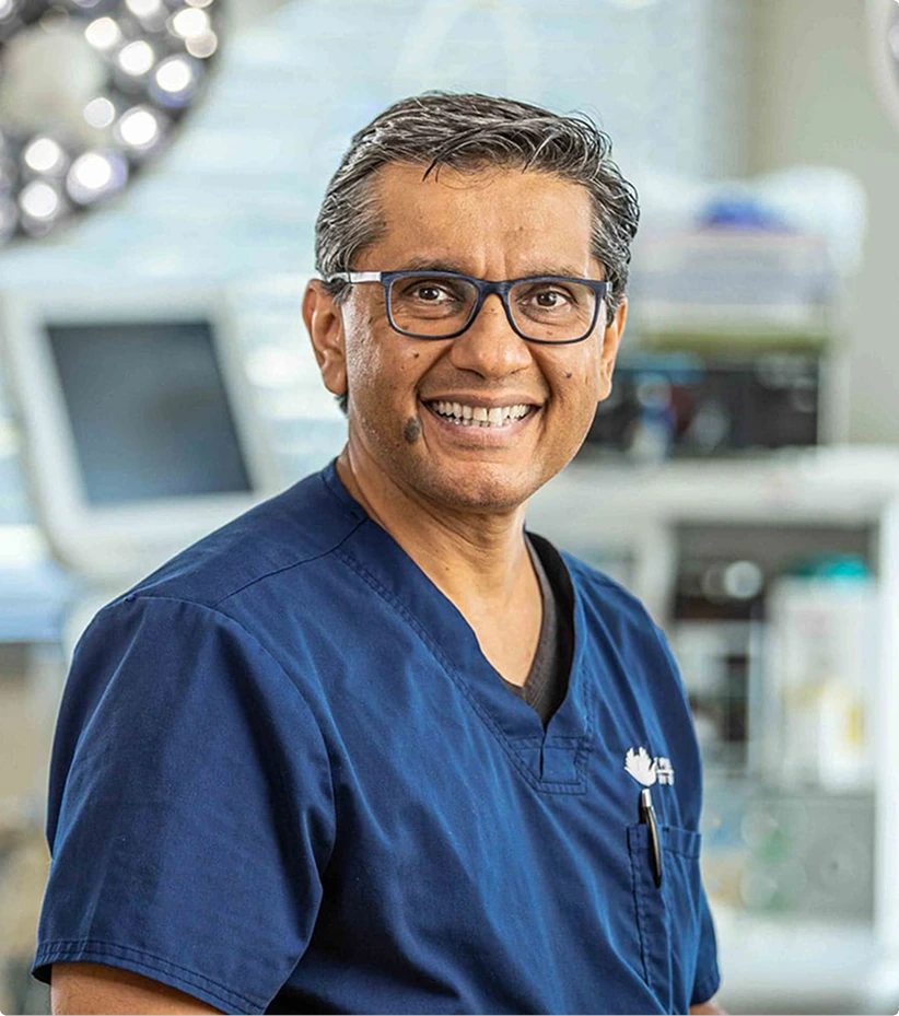 Plastic surgeon wearing glasses and navy scrubs smiling in modern surgical suite