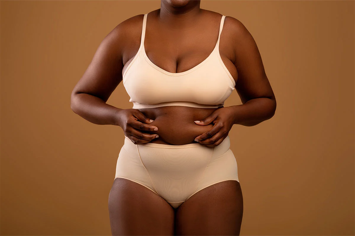 Person in beige underwear holding their abdomen against tan background