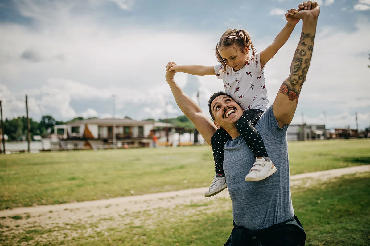 Woman lifting a young child in the air while smiling outdoors in a grassy field