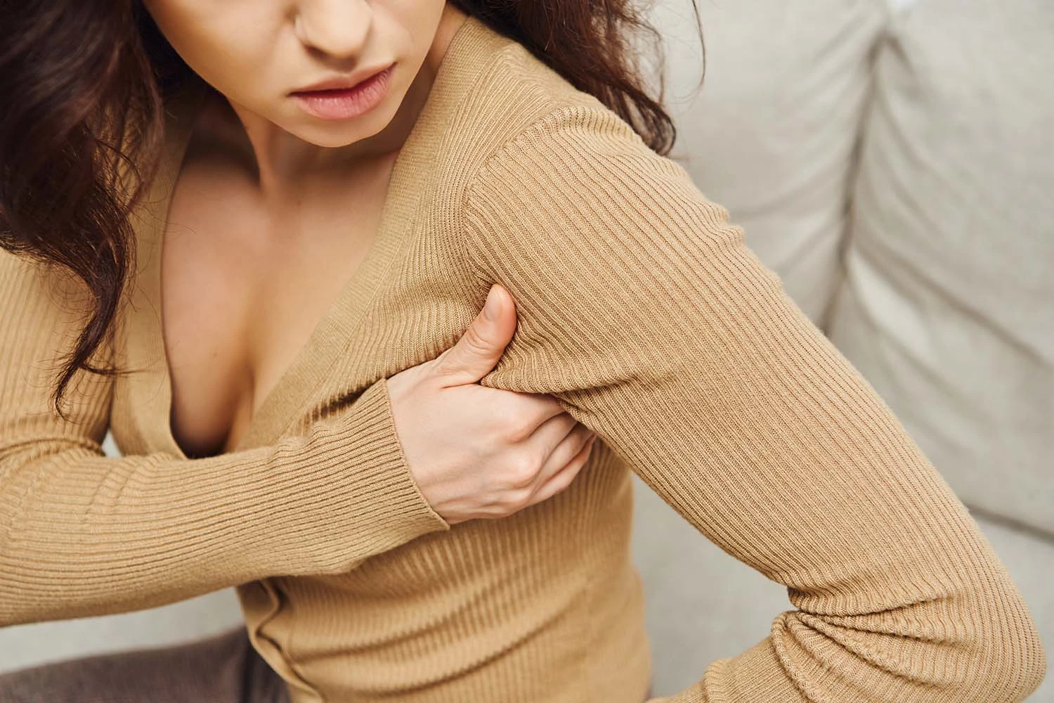 Woman in beige ribbed sweater touching her shoulder, with another person partially visible behind her