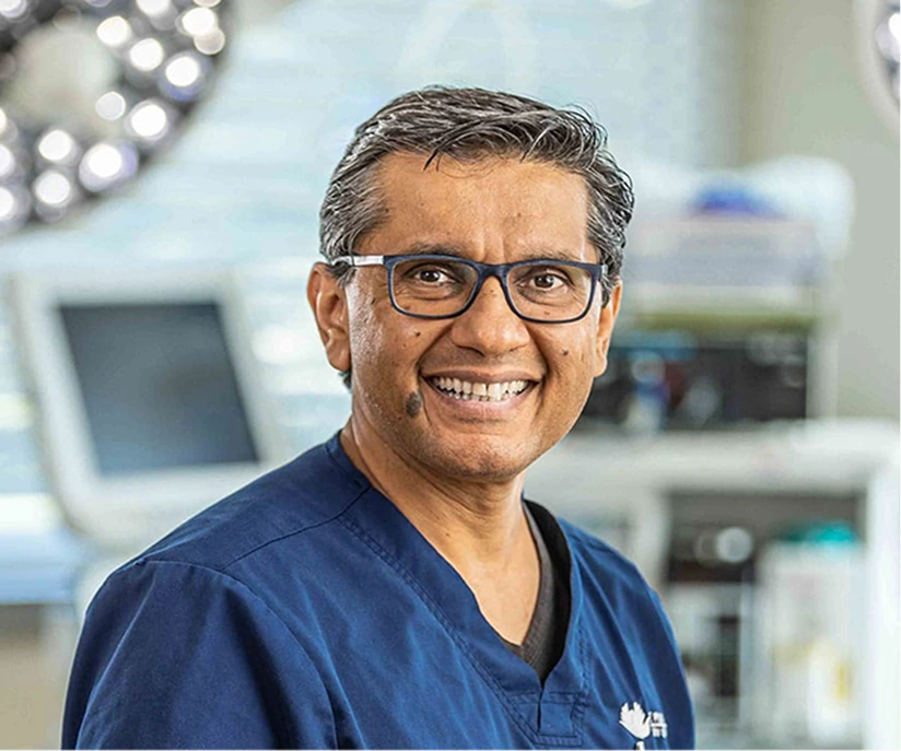 Surgeon in blue scrubs and glasses smiling in modern operating room