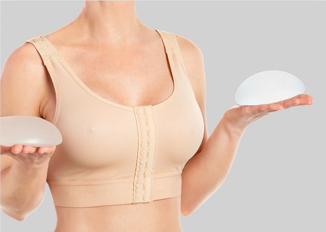 Woman wearing post-operative compression bra holding silicone breast implants in both hands