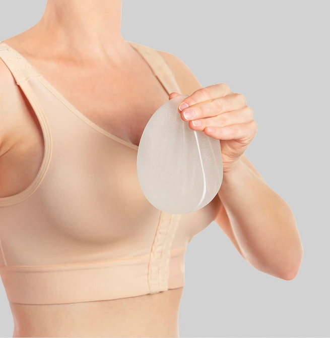 Woman in compression garment holding silicone breast implant