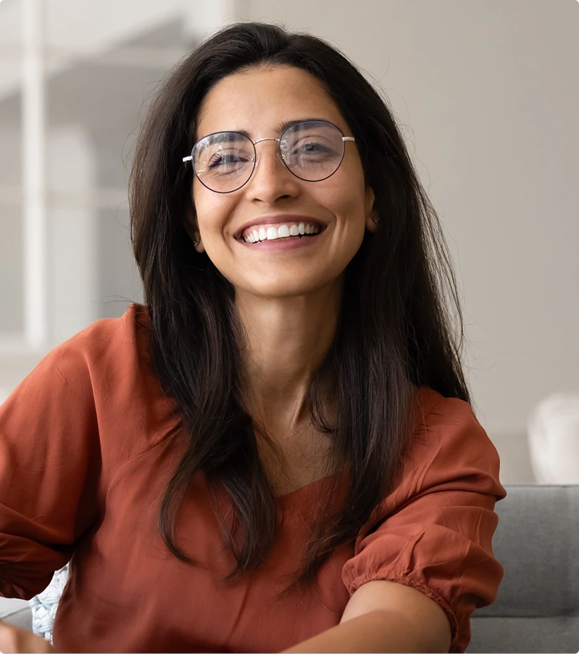 Woman wearing glasses and rust-colored shirt smiling indoors