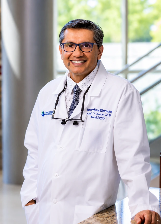 Plastic surgeon Dr. Amit V. Kacker in white coat with stethoscope, smiling in modern office setting