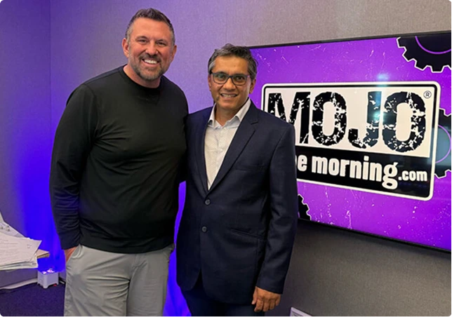 Two men posing together in front of a WOJO radio station logo on purple backdrop