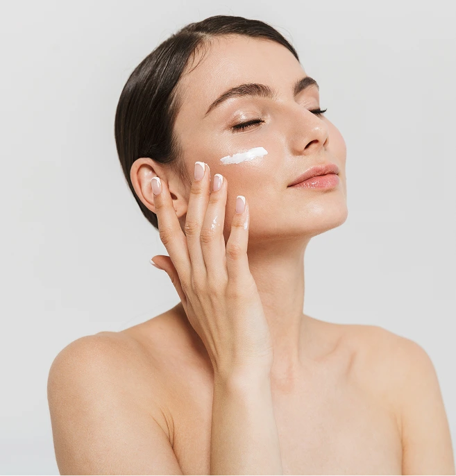 Woman applying skincare product to cheek with eyes closed