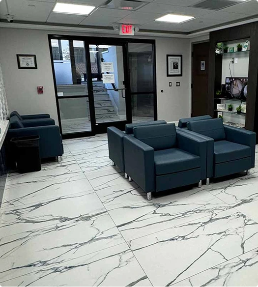 Waiting room with blue upholstered seating, glass doors, and marble flooring