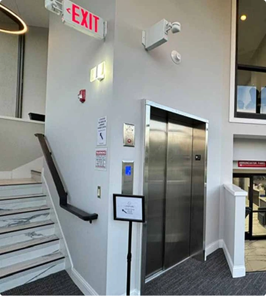 Clinical hallway with elevator, exit sign, and stairs in medical facility