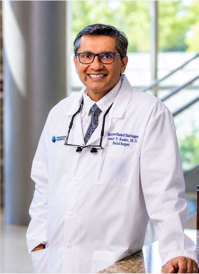 Amit V. Kacker, M.D. in white coat with stethoscope smiling at camera in clinical setting