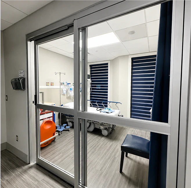 Surgical suite with glass doors, medical equipment, orange container, and examination table visible inside