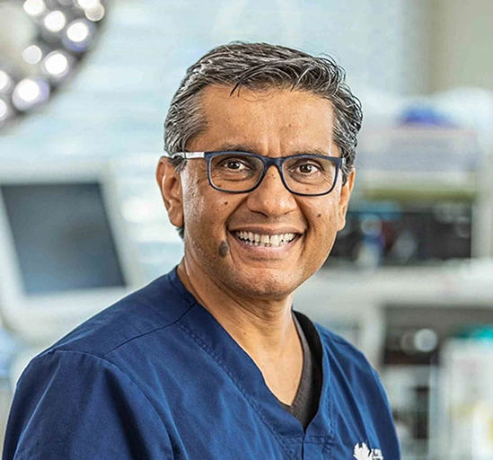 Dr. Shaher W. Khan smiling in surgical scrubs inside an operating room