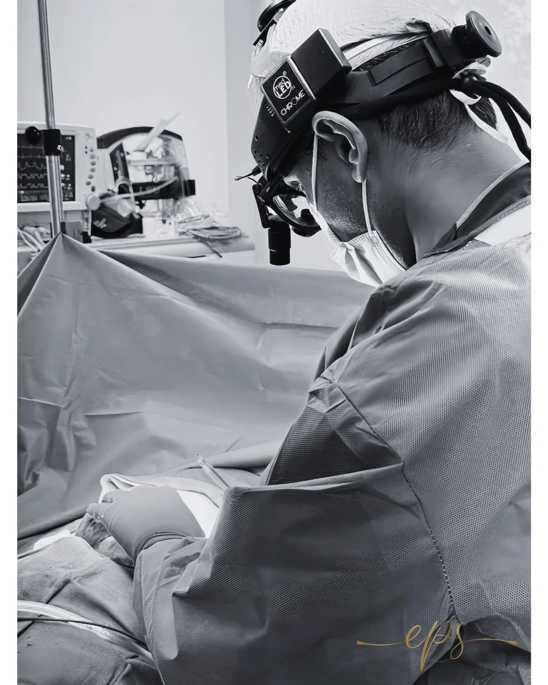 Surgeon wearing surgical loupes and headlight examining a patient's chest during breast implant explant procedure
